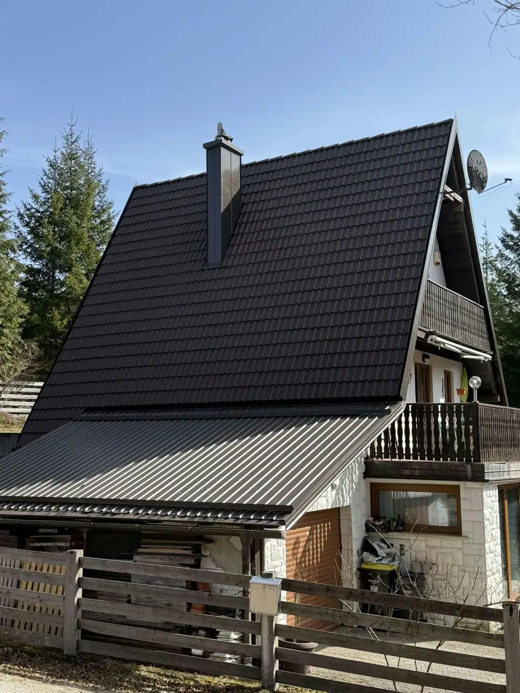 Dokončana temna kritina na strmi strehi vikend hiše s kovinskim nadstreškom