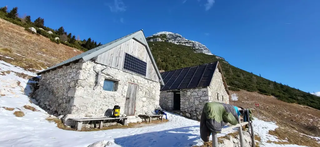 Planinska kamnita koča z obnovljeno streho pod gorskim vrhom